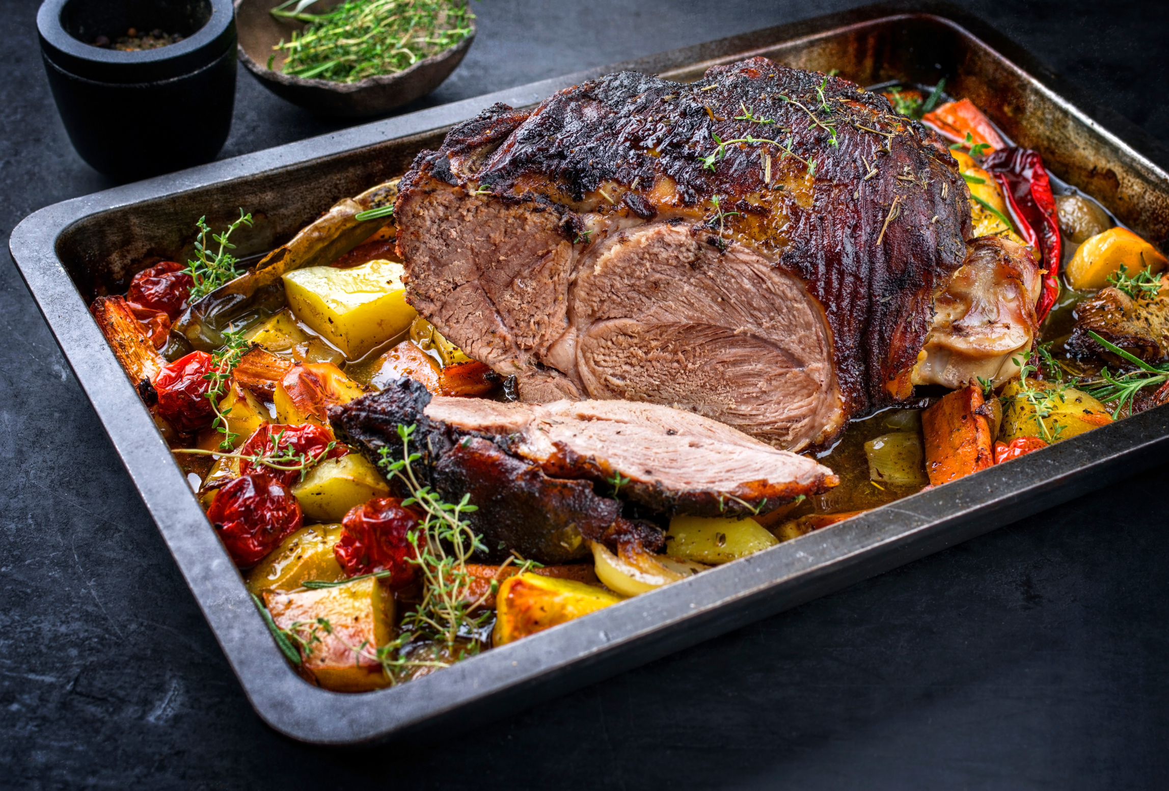 Traditioneller gegrillter Lammbraten aufgeschnitten mit Tomaten und Bratkartoffel als closeup auf einem Tablett
